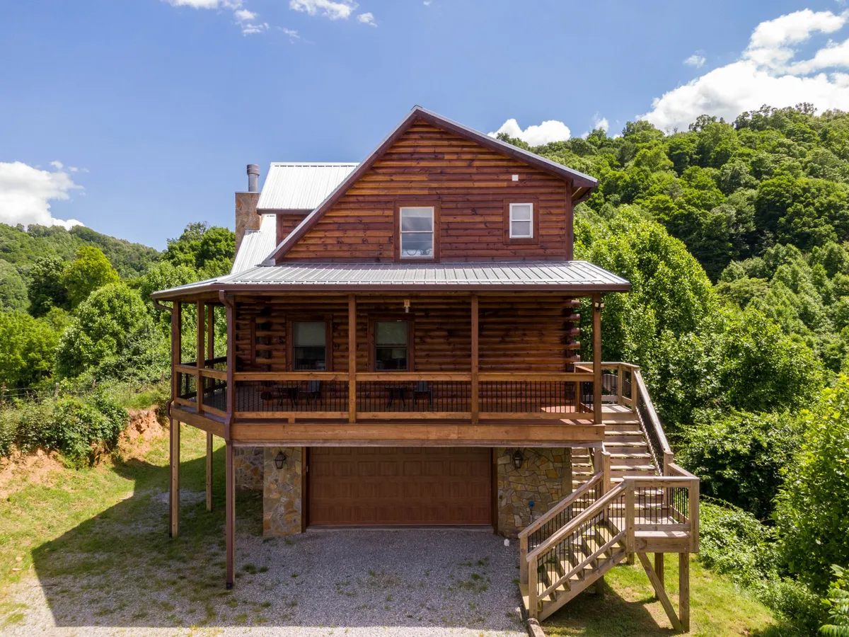 A view of the log cabin’s large front porch, surrounded by lush greenery and open space. The porch provides ample room for friends or small groups to gather, framing the home as a welcoming and private retreat away from the crowds.