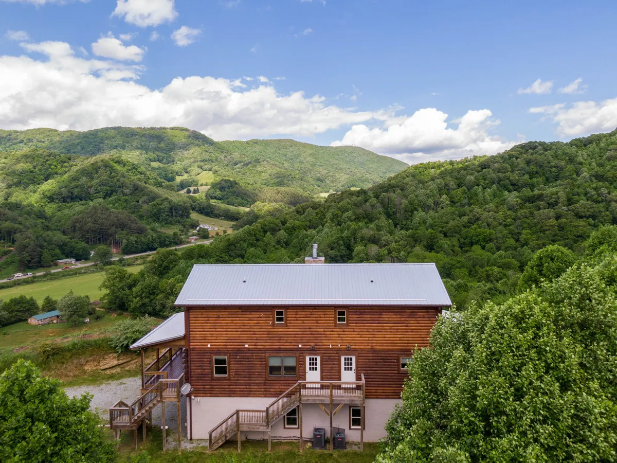 The exterior of a wooden cabin set against a dramatic mountain backdrop, with green trees and a spacious deck area in the foreground. This image emphasizes the home’s location amid natural beauty and hints at outdoor adventures such as hiking, nature observation, and gathering with friends or family.