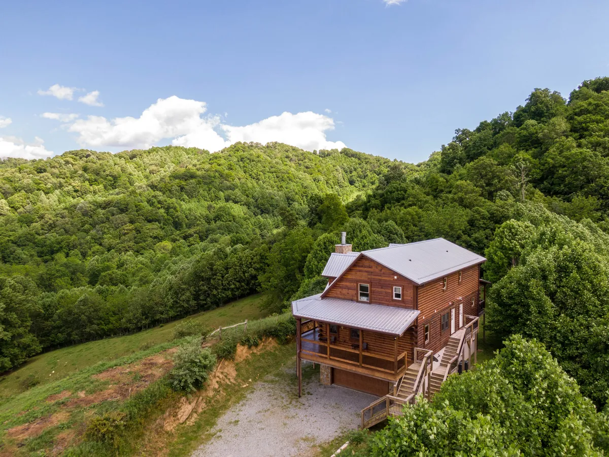 A picturesque wooden cabin nestled among tall trees with a dramatic mountain landscape in the background. The inviting porch and natural surroundings create a sense of adventure and connection to the outdoors, ideal for families wanting to explore and relax in nature.