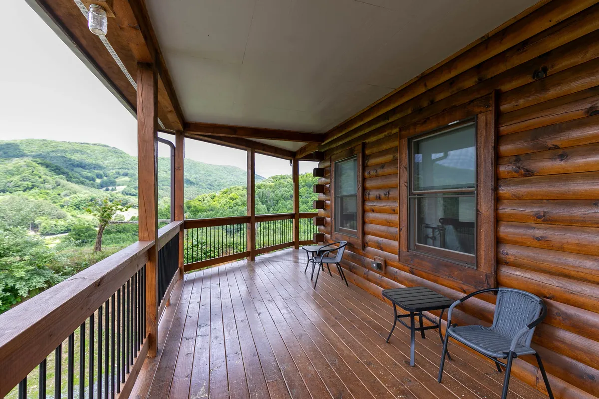 A spacious wooden deck overlooks sweeping mountain vistas, featuring comfortable outdoor seating. The area is bathed in natural light, making it ideal for morning coffee, evening conversations, or simply relaxing after a day of outdoor adventure. The setting is tranquil, with nature front and center.