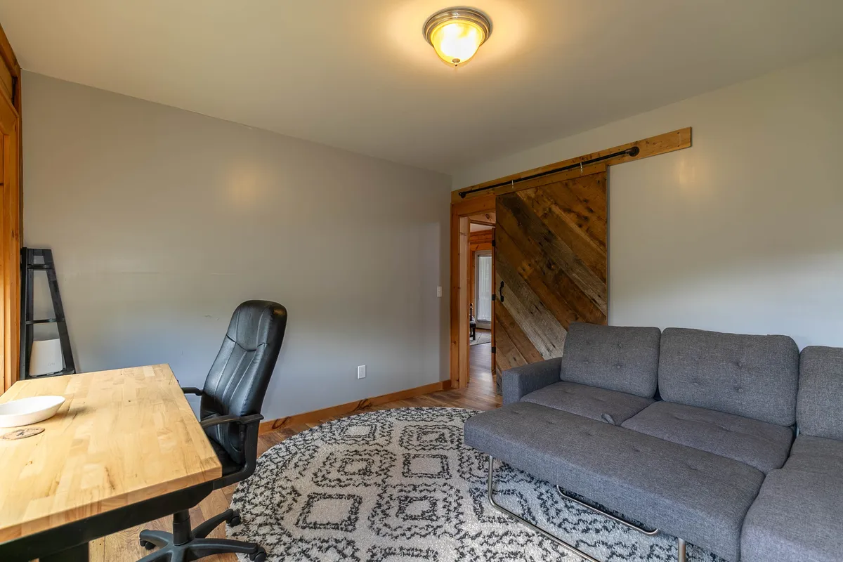 A warm, multipurpose office space featuring a desk, a plush sofa, a stylish rug, and a sliding door for privacy. The cozy ambiance makes it perfect for both focused work and restful sleep as an extra guest space.