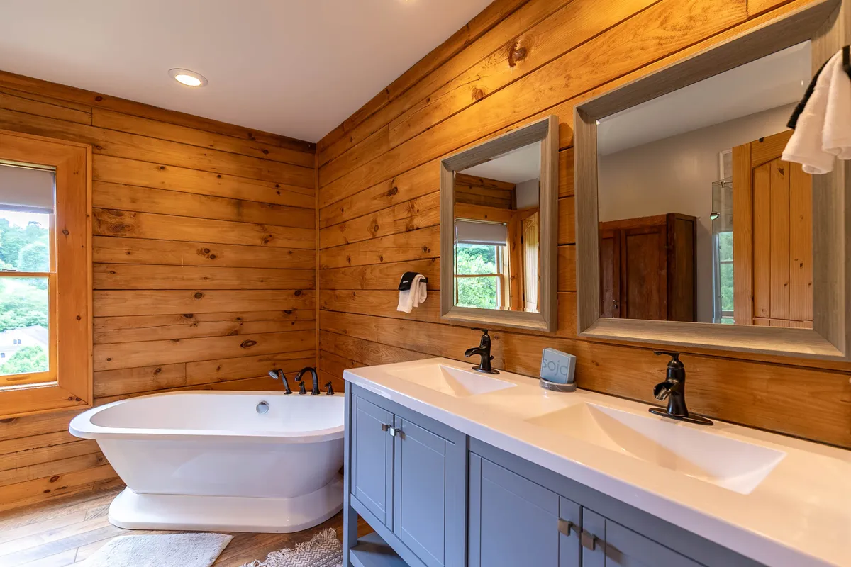A spa-inspired bathroom with a freestanding soaking tub, double sink vanity, mirrors, and wood paneling. The calm atmosphere and luxurious fixtures invite relaxation and self-care, capturing the essence of a private sanctuary.