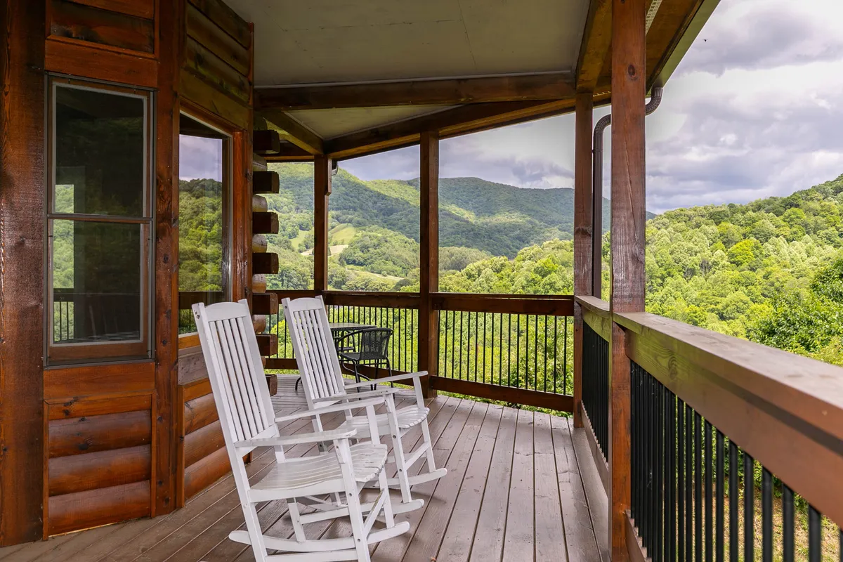 A pair of classic rocking chairs sit atop a wooden deck, framed by an expansive mountain vista beyond the railing. The scene exudes tranquility, with soft natural light perfect for relaxation or quiet contemplation.