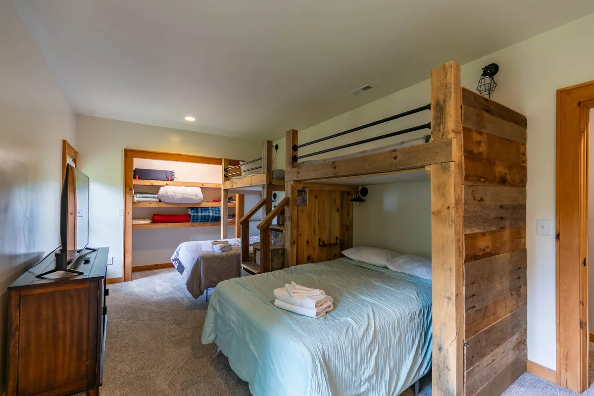A spacious bunk room with two sets of twin-over-full bunk beds, a double bed, a TV, and wooden furnishings. Designed for comfort and fun, the layout is perfect for families and kids, with plenty of sleeping space and room for play.