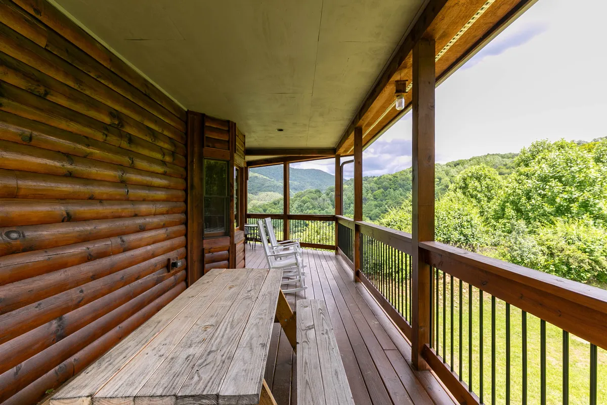 A rustic wooden deck furnished with a dining table and rocking chairs offers a sweeping, unobstructed mountain view. The railings and natural wood textures blend seamlessly with the surrounding landscape, inviting guests to relax outdoors at any time of day.