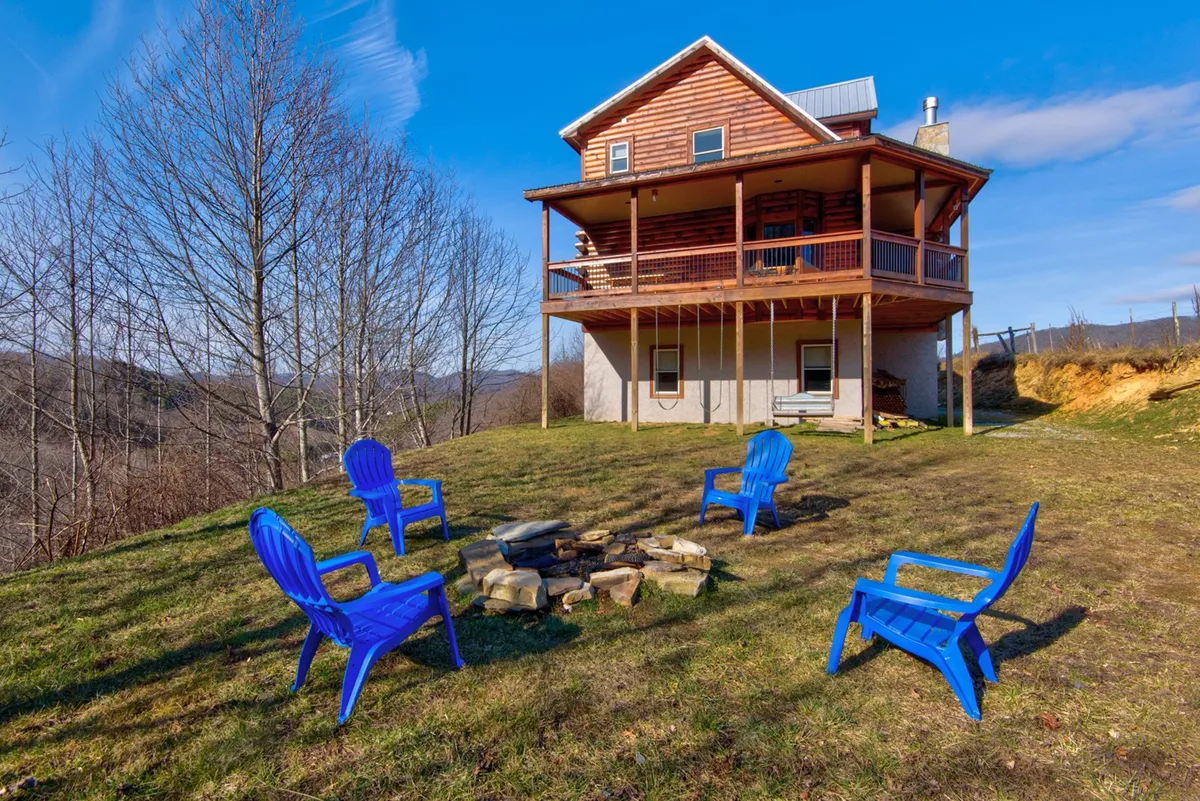 A cozy outdoor space featuring blue chairs arranged around a fire pit, with the wooden house and wide-open mountain landscape in view. The seating encourages group gatherings, while the fire pit adds warmth for year-round enjoyment.